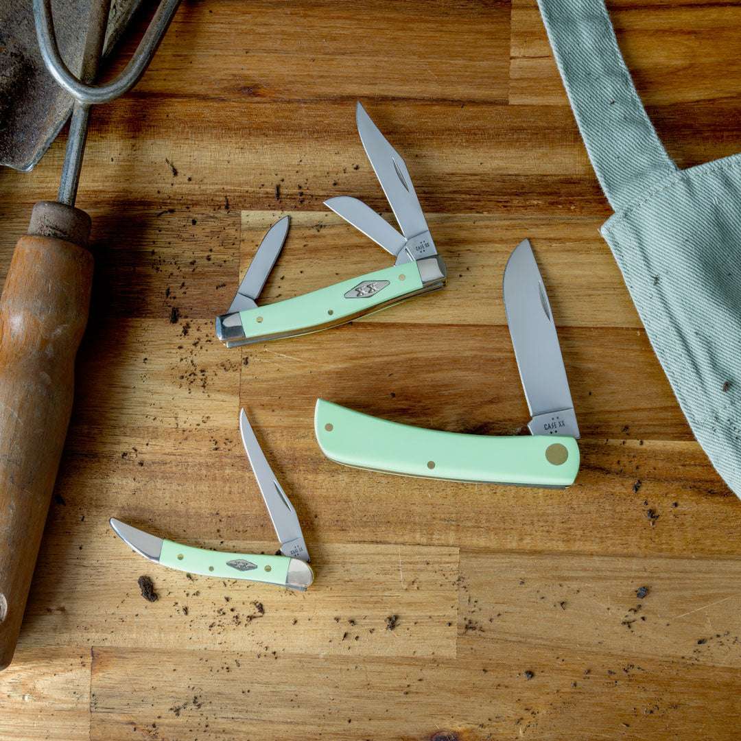 Case knife on a wooden surface with an apron and garden tool in the background.