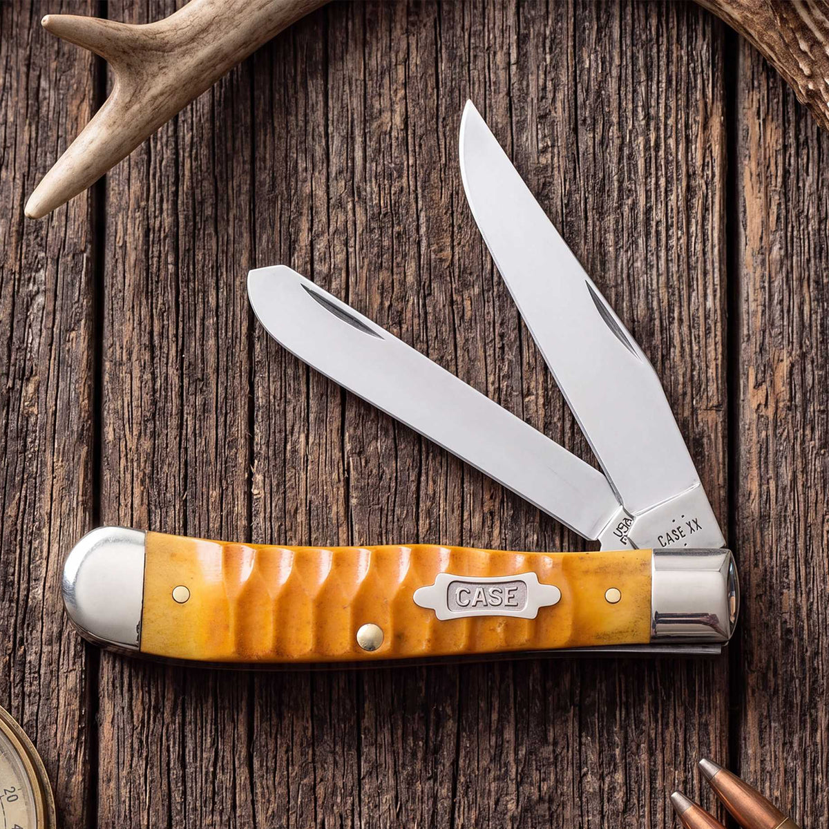 Gator Gig Persimmon Case knife on a wooden background with a compass and  bullets surrounding the knife.