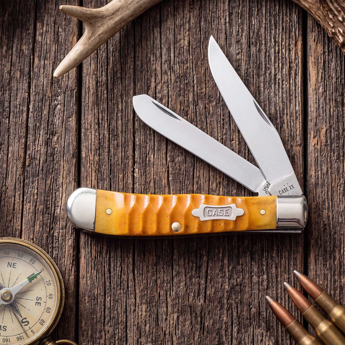 Orange Case knife on a wooden surface with bullets and a compass.