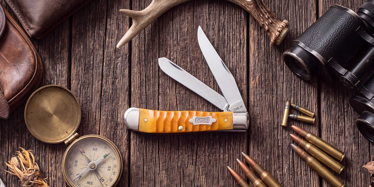 Orange Case knife on a wooden surface with bullets and a compass.