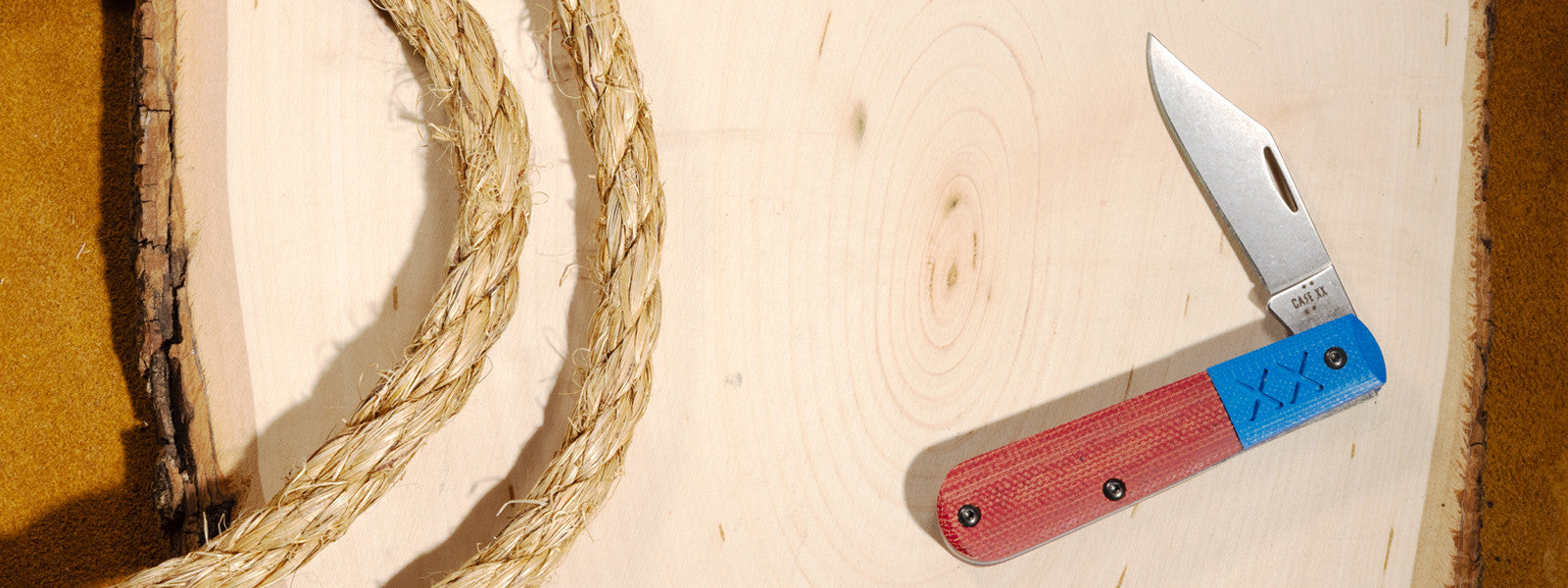 Case knife with red and blue handle on a wooden surface next to rope