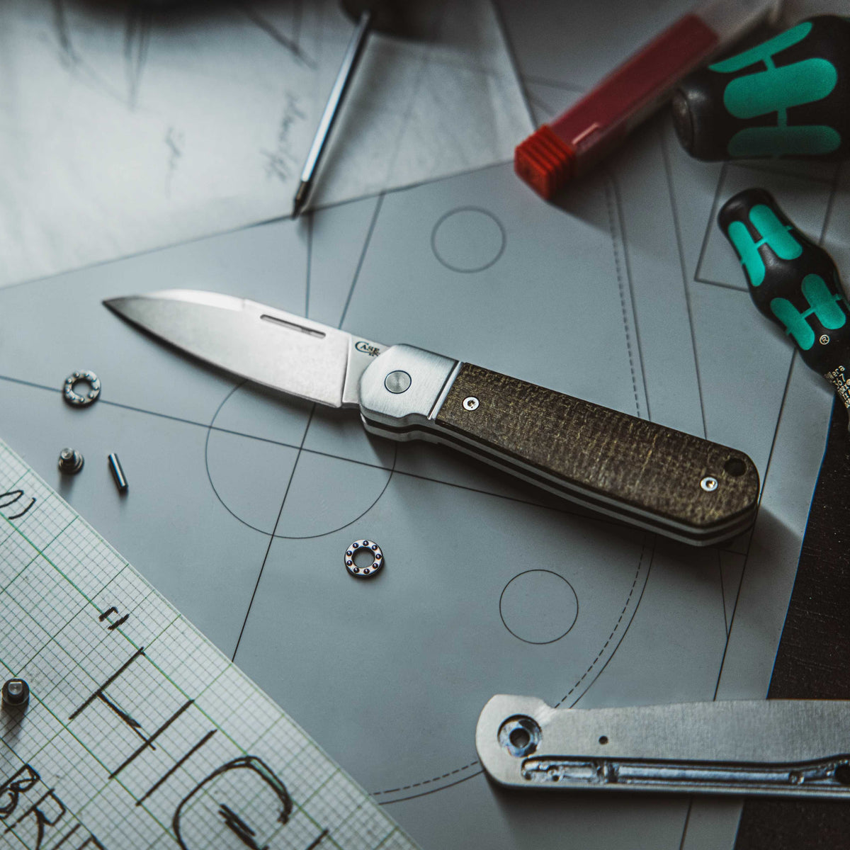 Case knife on a grey background with tools behind the knife.