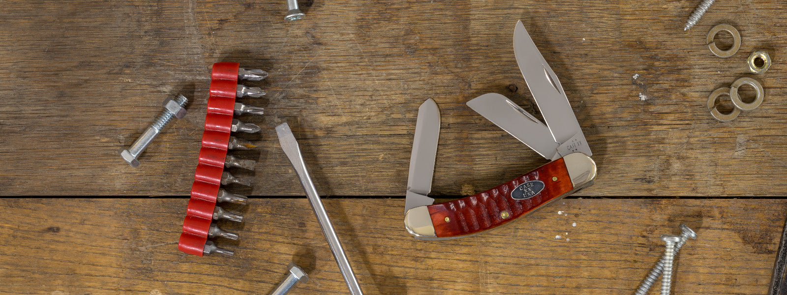 A Case knife is displayed on a rustic wooden plank surface alongside various metal hardware.