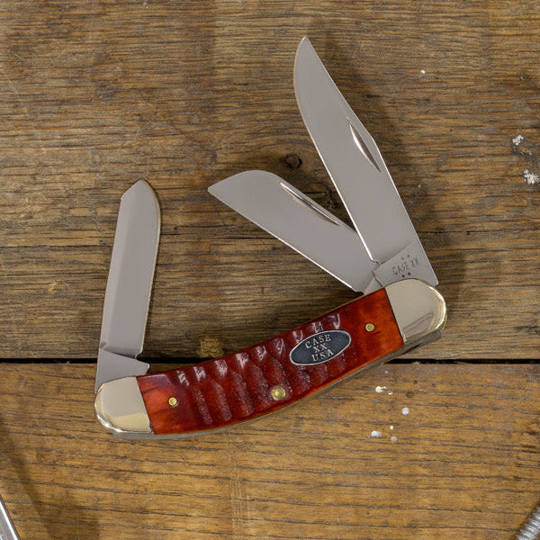 A Case knife is displayed on a rustic wooden plank surface alongside various metal hardware.