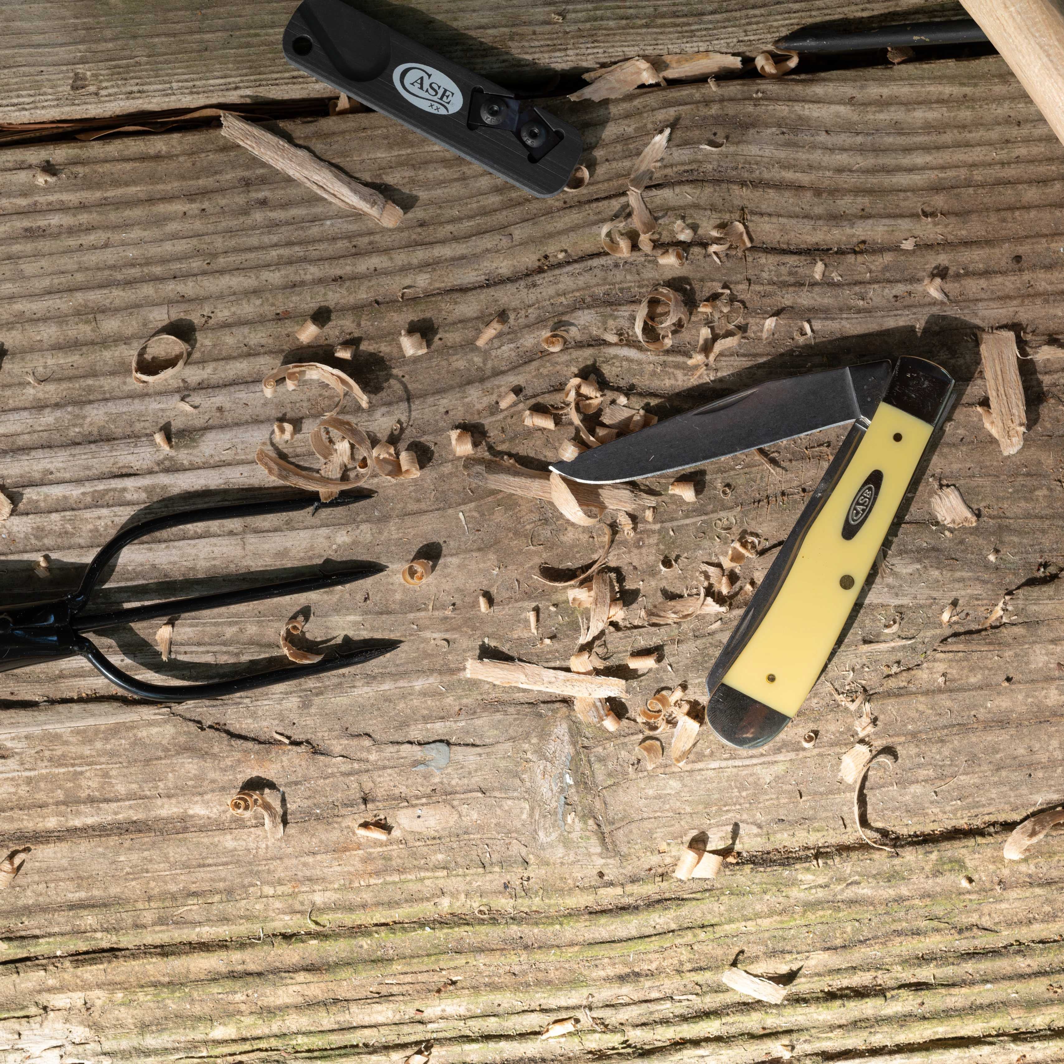 Yellow Case knife on a wooden surface with wood shavings laying around.