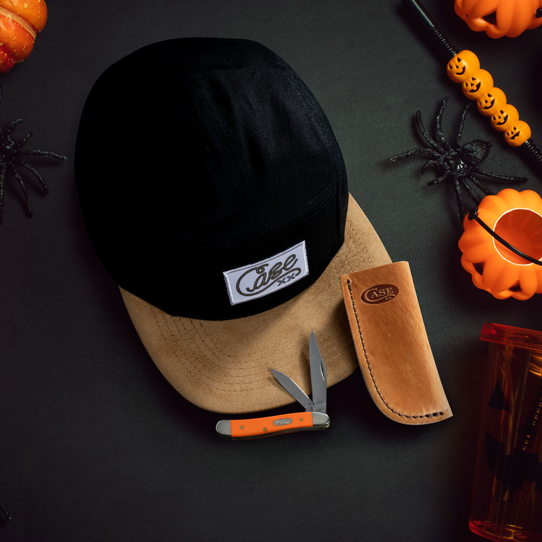 Case baseball cap, sheath, and pocket knife on Halloween background.