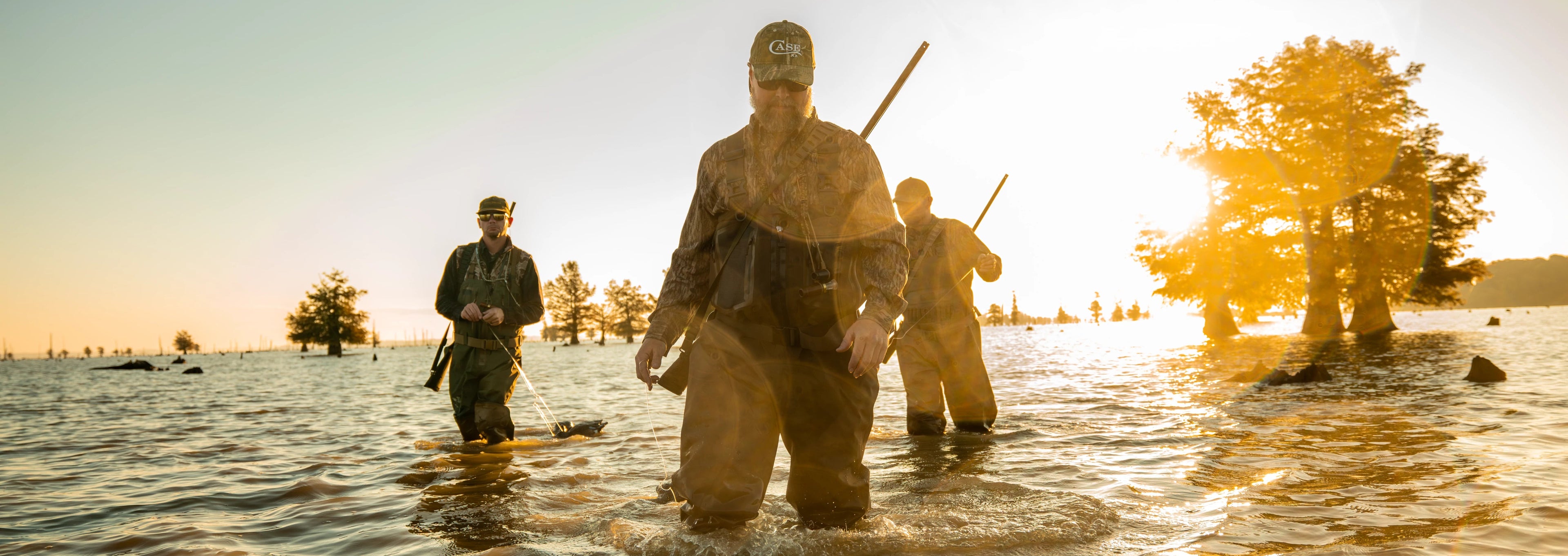 Three people wading through water at sunset with trees in the background