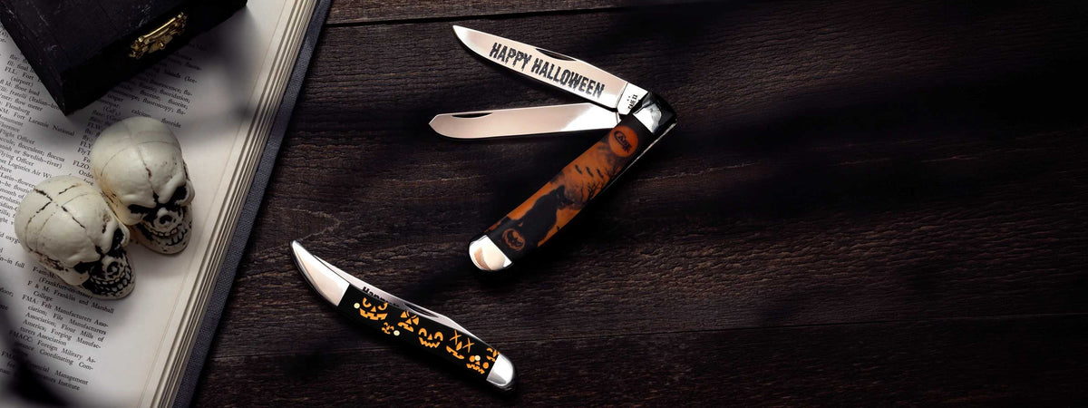 Two Case Halloween knives on a wooden surface with two skulls and a book in the background.
