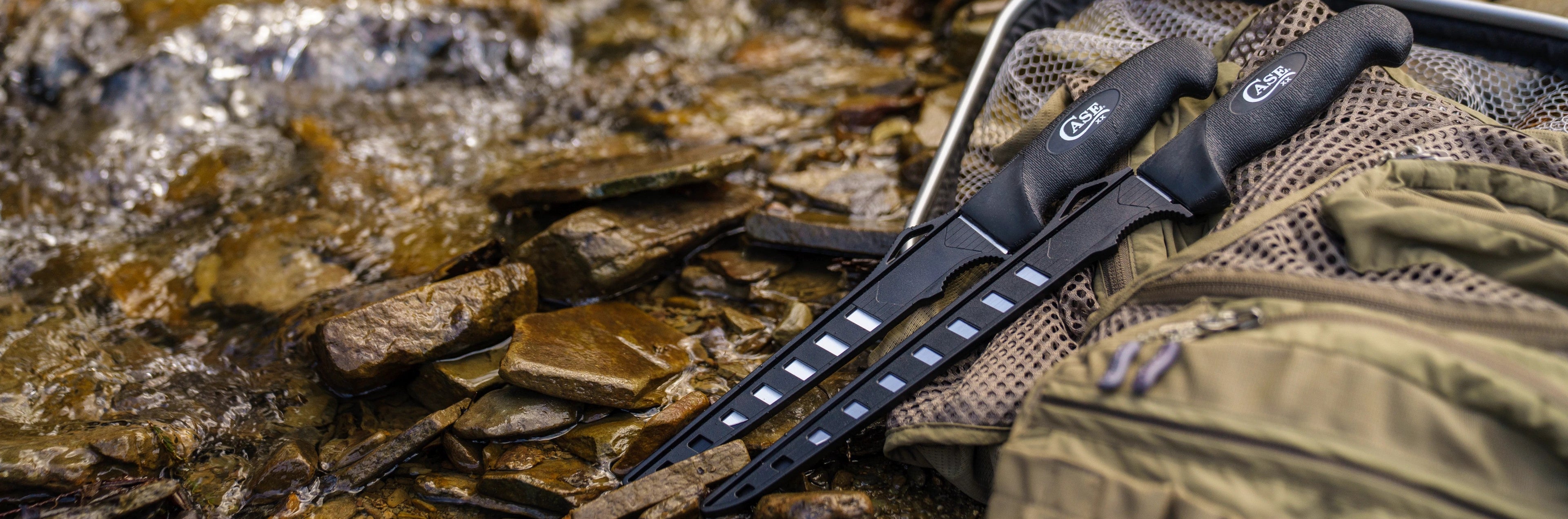 Two black Case knives on a rocky surface with a green bag in the background.