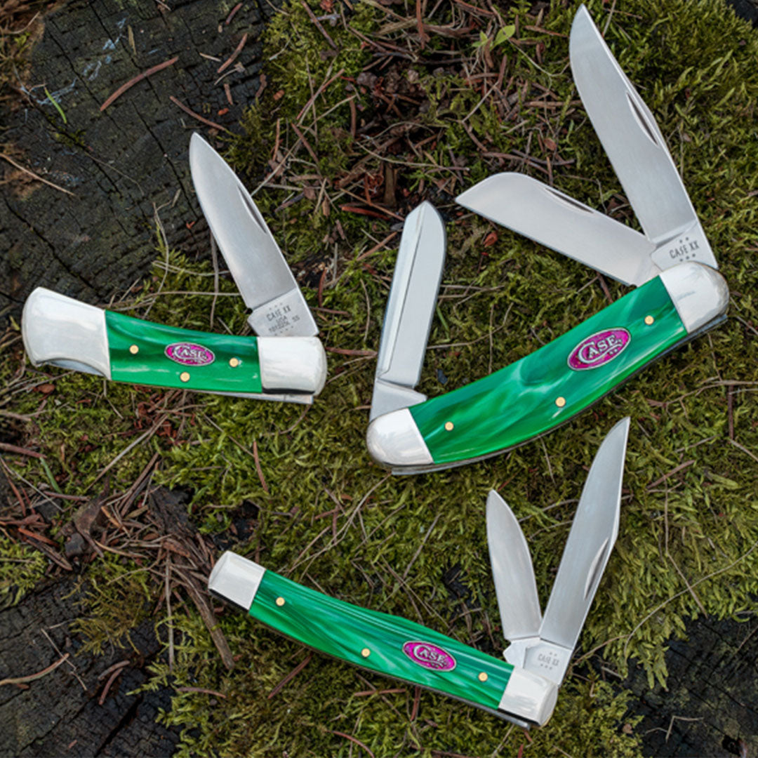 Three new Green Pearl Kirinite knives on a mossy tree stump.