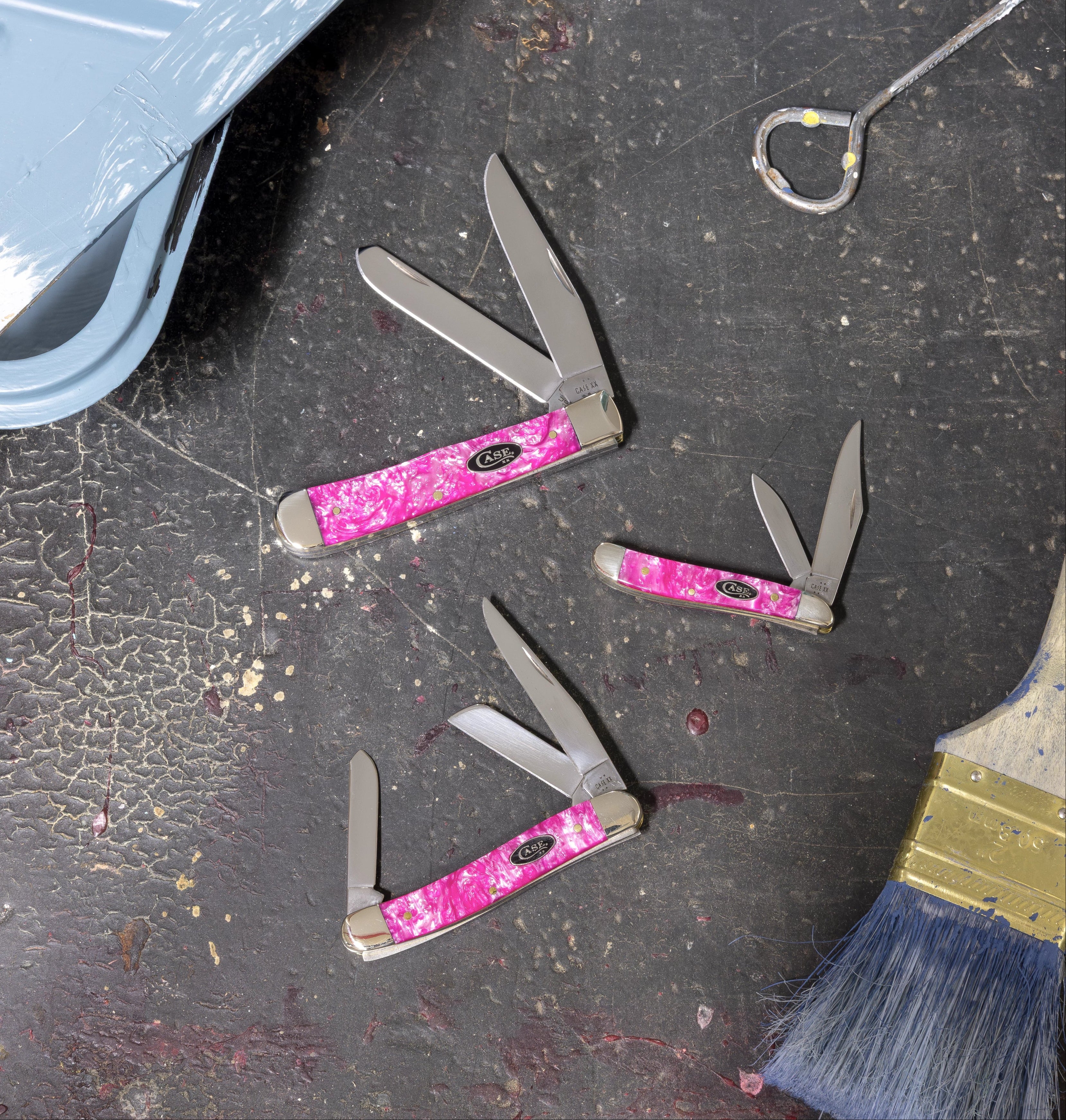 Three pink Case knives on a work bench with tools and paint