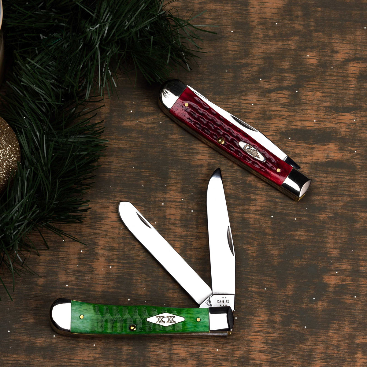 One red and one green Case knife on a wooden surface with greens in the background. 