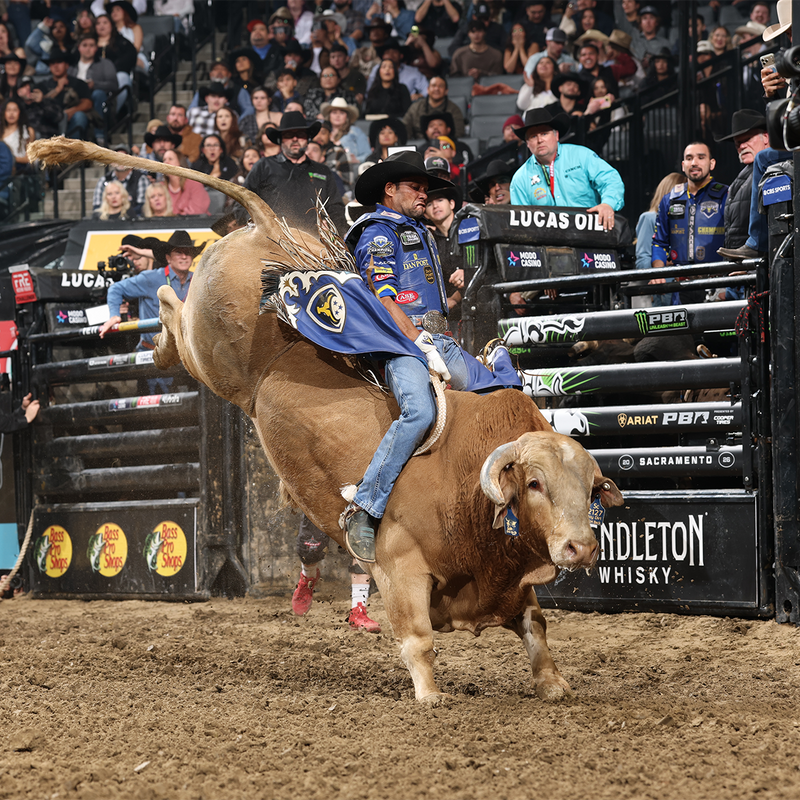 NASHVILLE STAMPEDE: A cowboy in a blue jacket and jeans rides a bucking brown bull during a rodeo event, with a crowd and arena barriers in the background. Visible sponsor logos include Lucas Oil, PBR, and Hendleton Whisky.