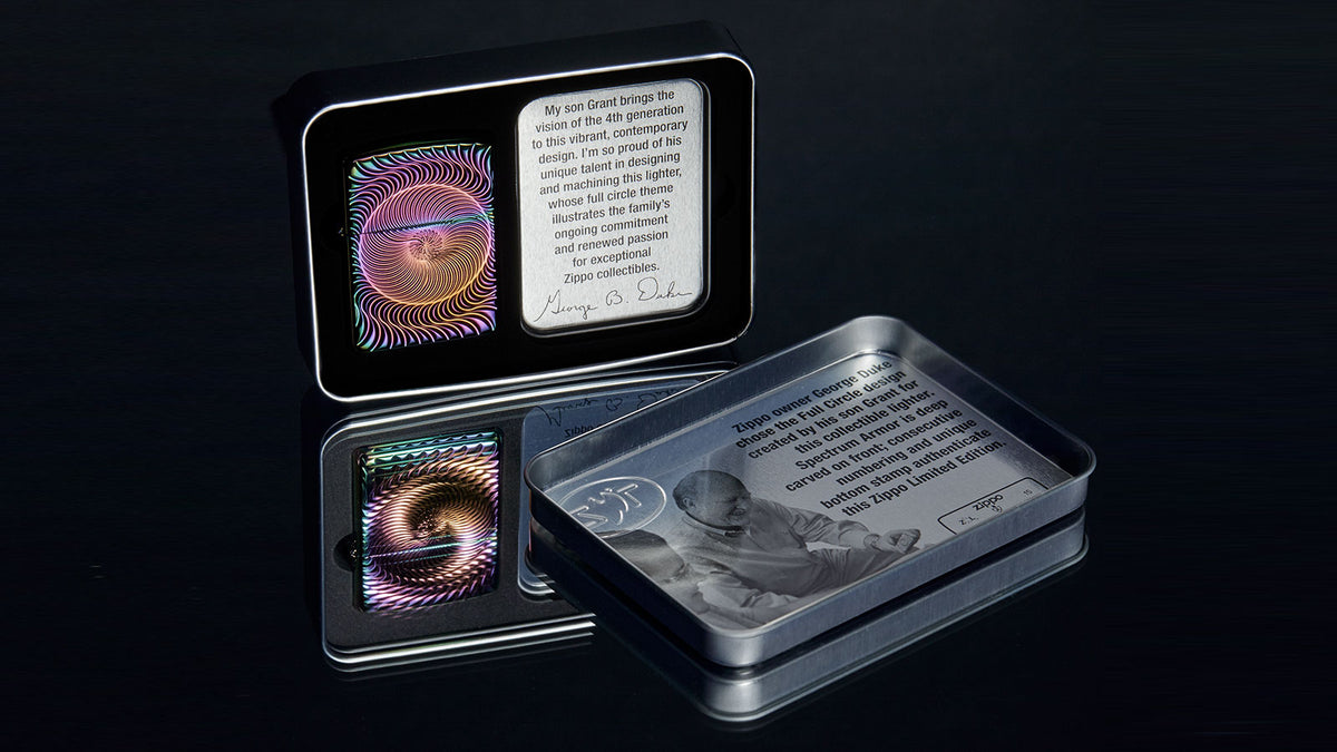 A decorative metal tin set displayed on a dark reflective surface, with one tin open to show a colorful lighter design and printed text, and another tin beside it showing a grayscale illustration and text.