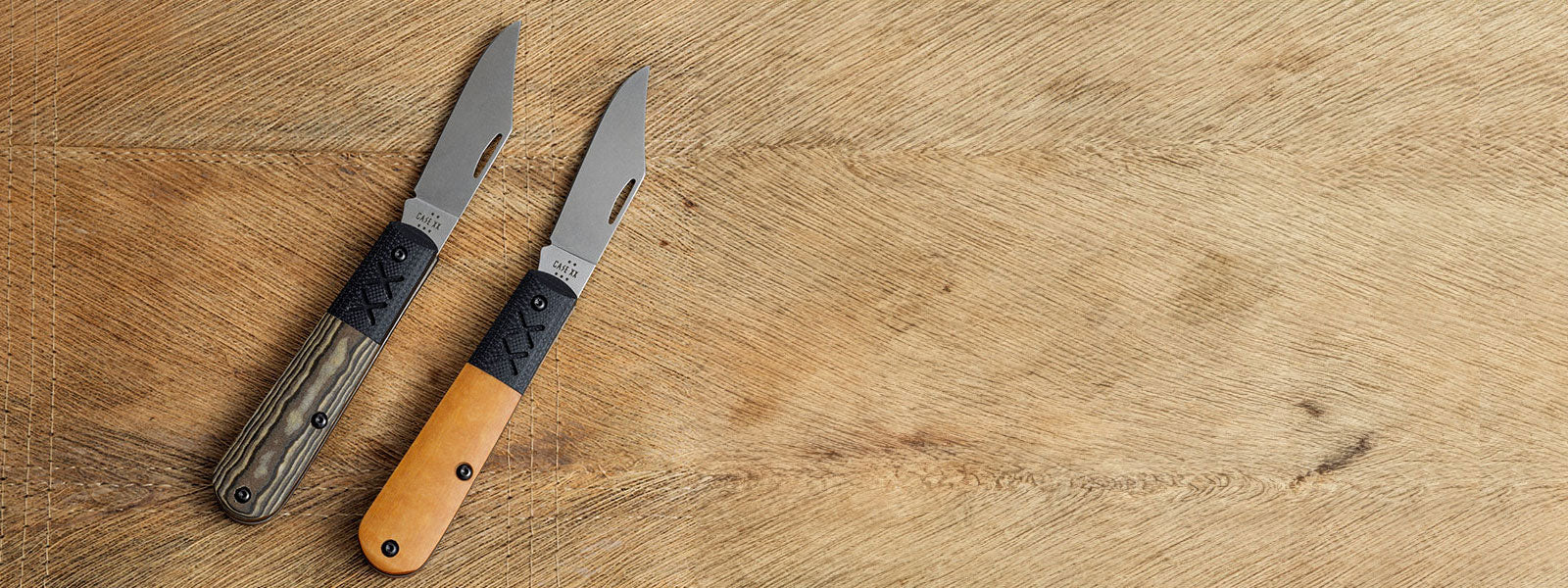 Two Crossroads Barlow knives with wooden handles on a wooden surface.