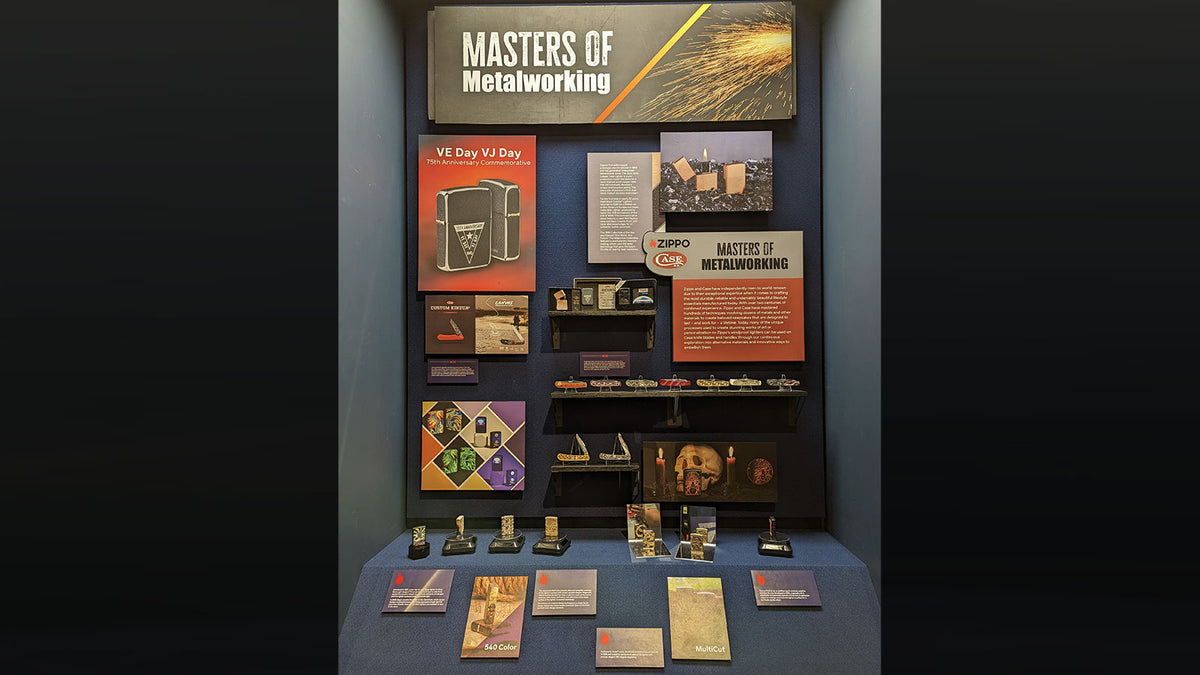 An indoor exhibition display titled "MASTERS OF Metalworking" with multiple posters, small objects, and printed materials arranged on a dark wall and table against a dark background.