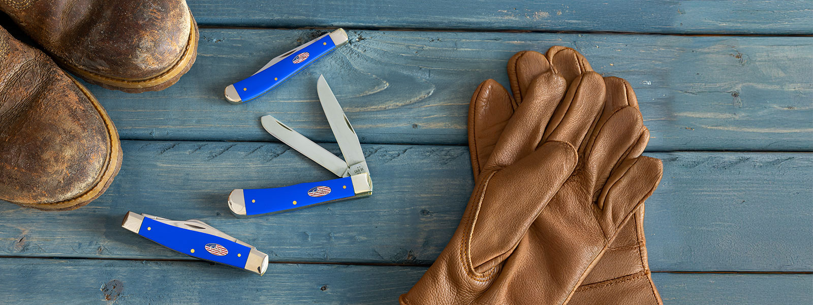 Brown leather boots and gloves with 3 Case knives on a wooden surface.