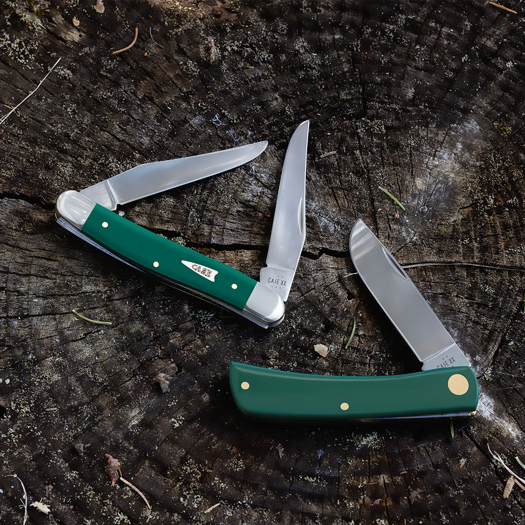 Two Smooth Spruce Green knives on a wooden surface.