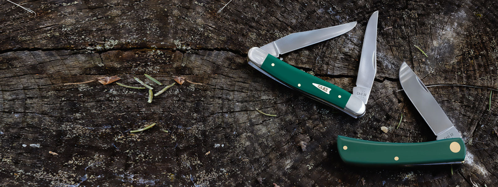 Two Smooth Spruce Green knives on a wooden surface.