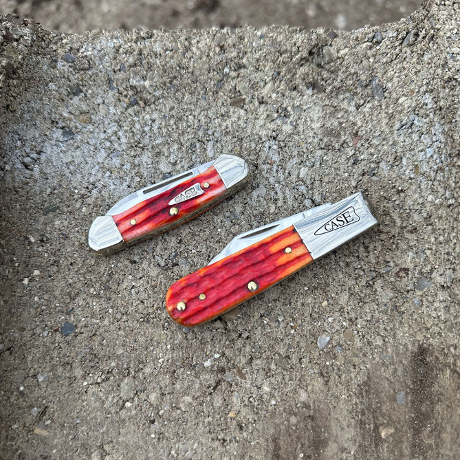 Two Case knives with red handles and silver blades on a concrete surface.