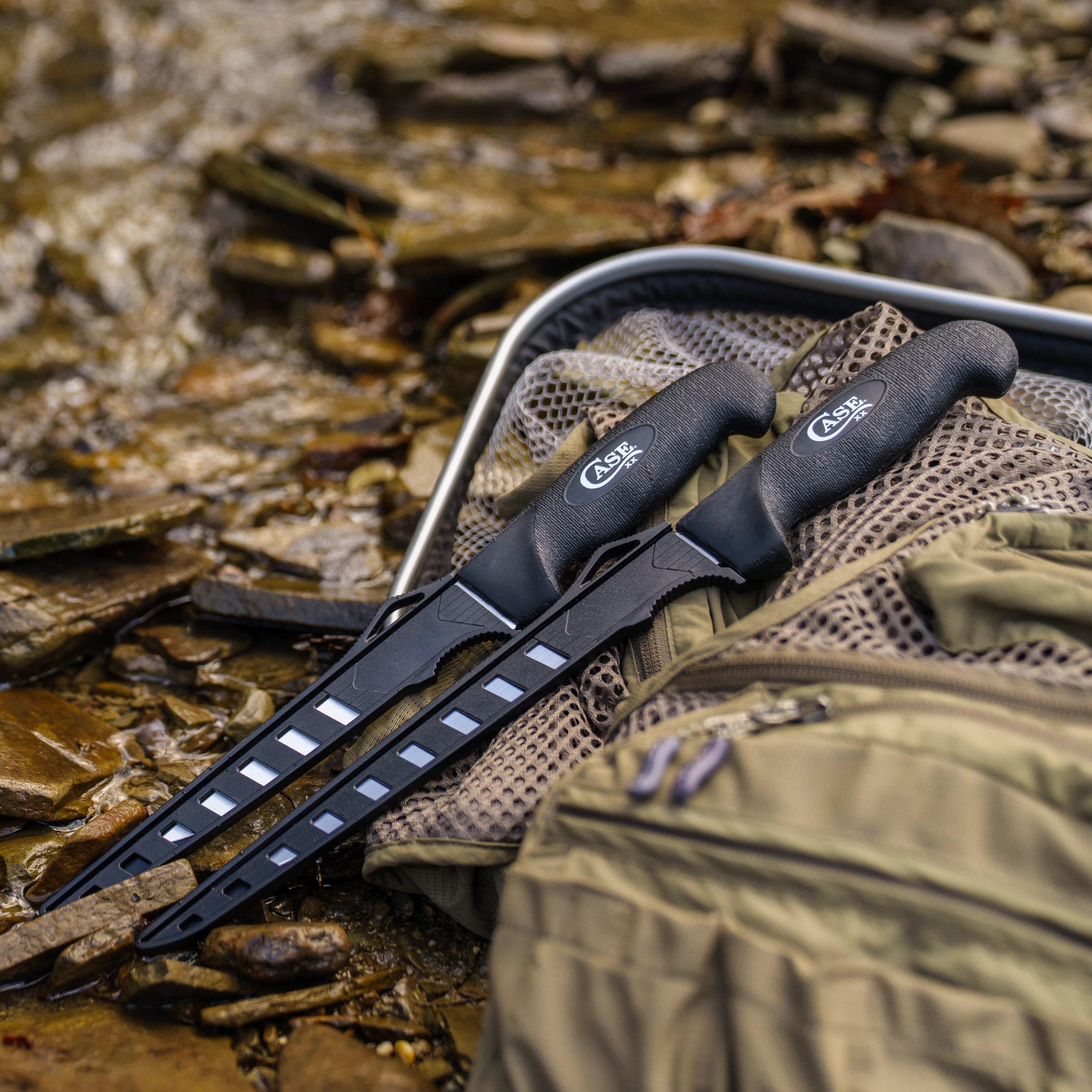 Two black Case knives on a rocky surface with a green bag in the background.