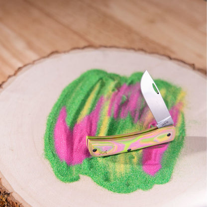 Case® | Crossroads™ Tropical Burl G-10 XR Sod Buster® Jr open with blade facing up on a wooden stump with color matched sand underneath.