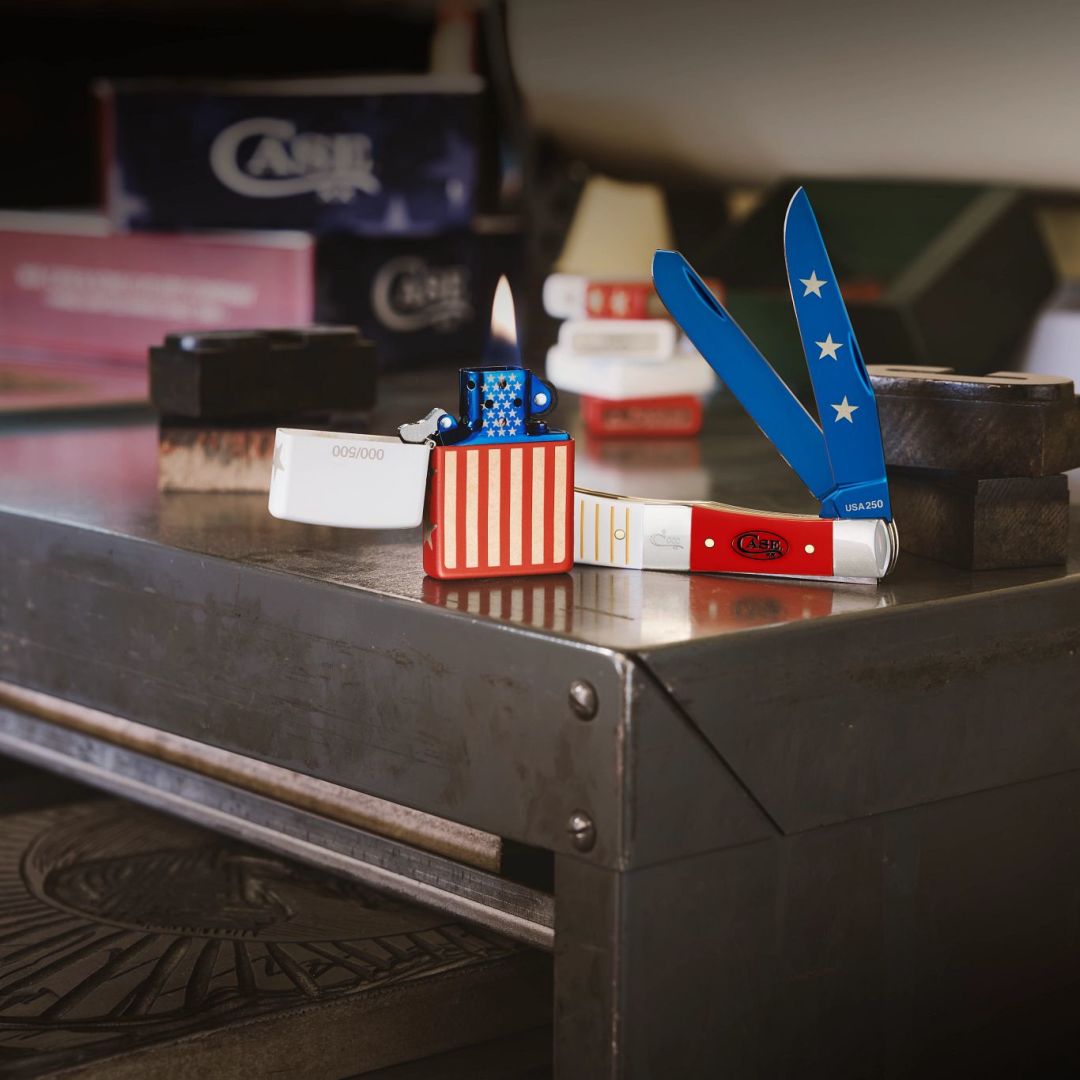 Lifestyle image of 2026 USA 250 Gift Set - Smooth White & Red Synthetic Center Bolstered Trapper w/ Lighter both standing on a cabinet with lighters and boxes in the background.