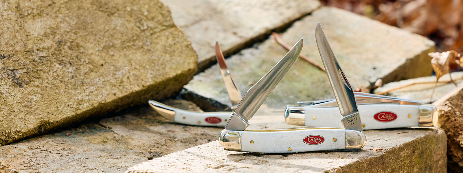 Three pocket knives on a stone surface with visible brand names.