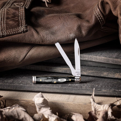 Lifestyle image of Buffalo Horn Jigged Baby Doc open and standing on a wooden board with dried leaves in front and a leather jacket behind it.