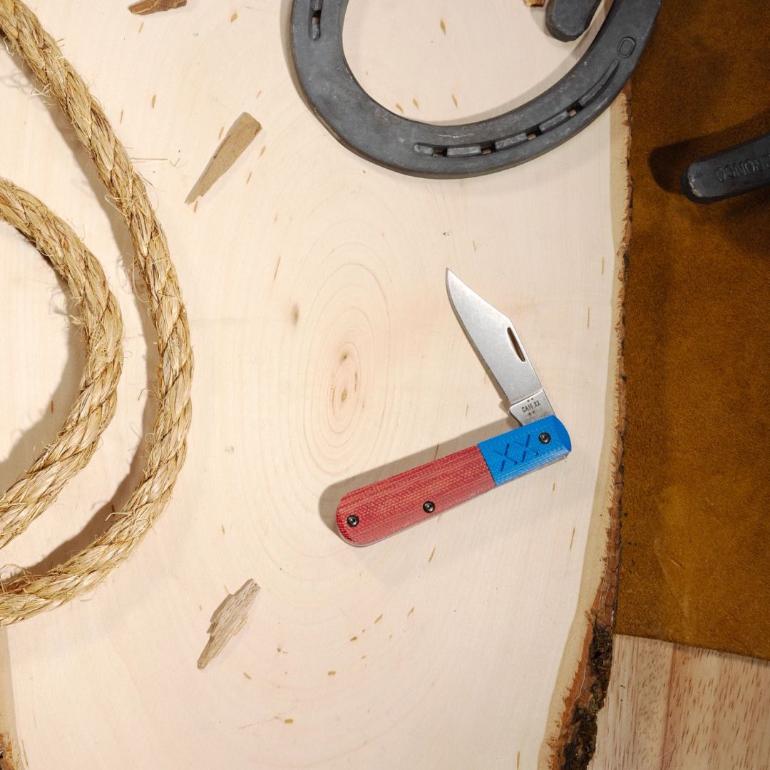 Lifestyle image of Crossroads™ Smooth Orange Canvas Laminate with Blue G-10 XR Barlow open with a horseshoe and rope next to it.